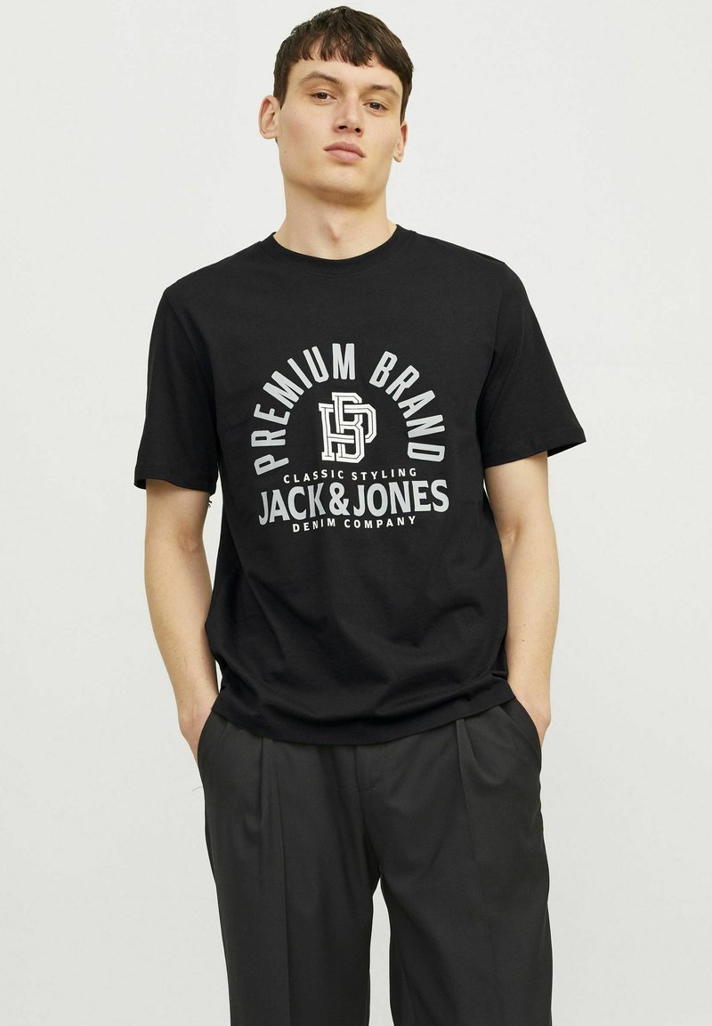 Juodos medvilnės marškinėliai su baltu spaudiniu, kuriame parašyta "Premium Brand" ir "Jack & Jones Denim Company." Trumpomis rankovėmis, apvaliu kaklu.