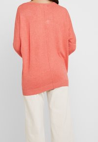 Korala dzianinowy sweter o luźnym kroju, z rękawami typu batwing, prążkowanym dekoltem i dołem, z detalem szwu na środku tyłu. W zestawie z jasnymi spodniami.