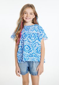 Top blu e bianco a fantasia con maniche corte, caratterizzato da un bordo in pizzo. Abbinato a pantaloni corti in denim, il modello ha capelli lunghi con ciocche colorate.