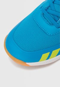 Μπλε αθλητικό παπούτσι με επάνω μέρος από πλέγμα με λεία υφή, σόλα από καουτσούκ και κίτρινα διακοσμητικά στο πλάι. Στρογγυλεμένος σχεδιασμός στο μπροστινό μέρος.