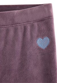 Tissu en polaire violet avec une texture lisse, comportant un accent de cœur brodé bleu clair près du bord supérieur.