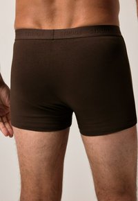 Boxers en coton brun avec une texture lisse et une ceinture élastique de marque, offrant un ajustement confortable et une couverture de jambe courte.