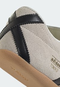 Gray suede shoe with black leather accents, textured sole, stitched detailing, and "adidas Tokyo" logo embossed on the side.