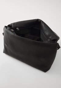 Crna kožna torba sa mekanom teksturom, zatvaranjem na patentni zatvarač i prostranim unutrašnjim prostorom. Ima kružne akcentne detalje sa strane.