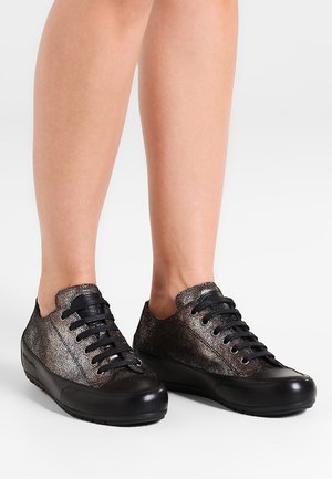 Skinnende sorte og metalliske lave sneakers med sorte snørebånd, båret på bare ben, vist mod en ensartet lys baggrund.