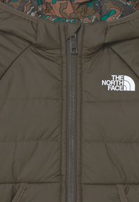 Polstret olivengrøn jakke med lynlås foran, med et logo på brystet og foring i camouflage-mønster.