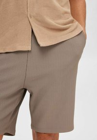 Chemise beige texturée avec détail de bouton associée à un short côtelé marron clair. Les deux vêtements présentent des matériaux doux et confortables ainsi que des coupes décontractées.