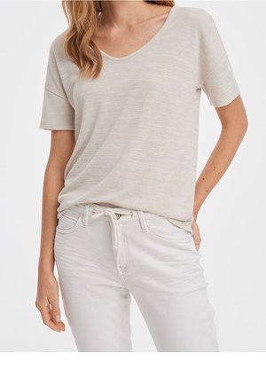 Beige kortærmet top med V-halsdesign, lavet af let materiale. Kombineret med lyse bukser, der har en justerbar snøre.