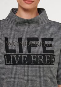 Grijze geblokte sweatshirt met een hoge kraag. Bevat zwarte tekst "WONDERFUL LIFE" en "LIVE FREE" in contrasterende teksten en versieringen.