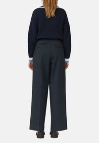 Marineblauwe gebreide trui met lichtblauwe gestreepte manchetten, in combinatie met donker gestreepte brede broek met zichtbare achterzakken en zwarte schoenen.