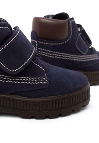 Scarpe in suede blu navy con punta rotonda, dettagli in pelle marrone, cintura in velcro, cuciture bianche e suola in gomma nera testurizzata.