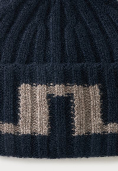 Gros plan d'un bonnet noir côtelé présentant un motif géométrique beige tricoté avec des lignes verticales et horizontales.