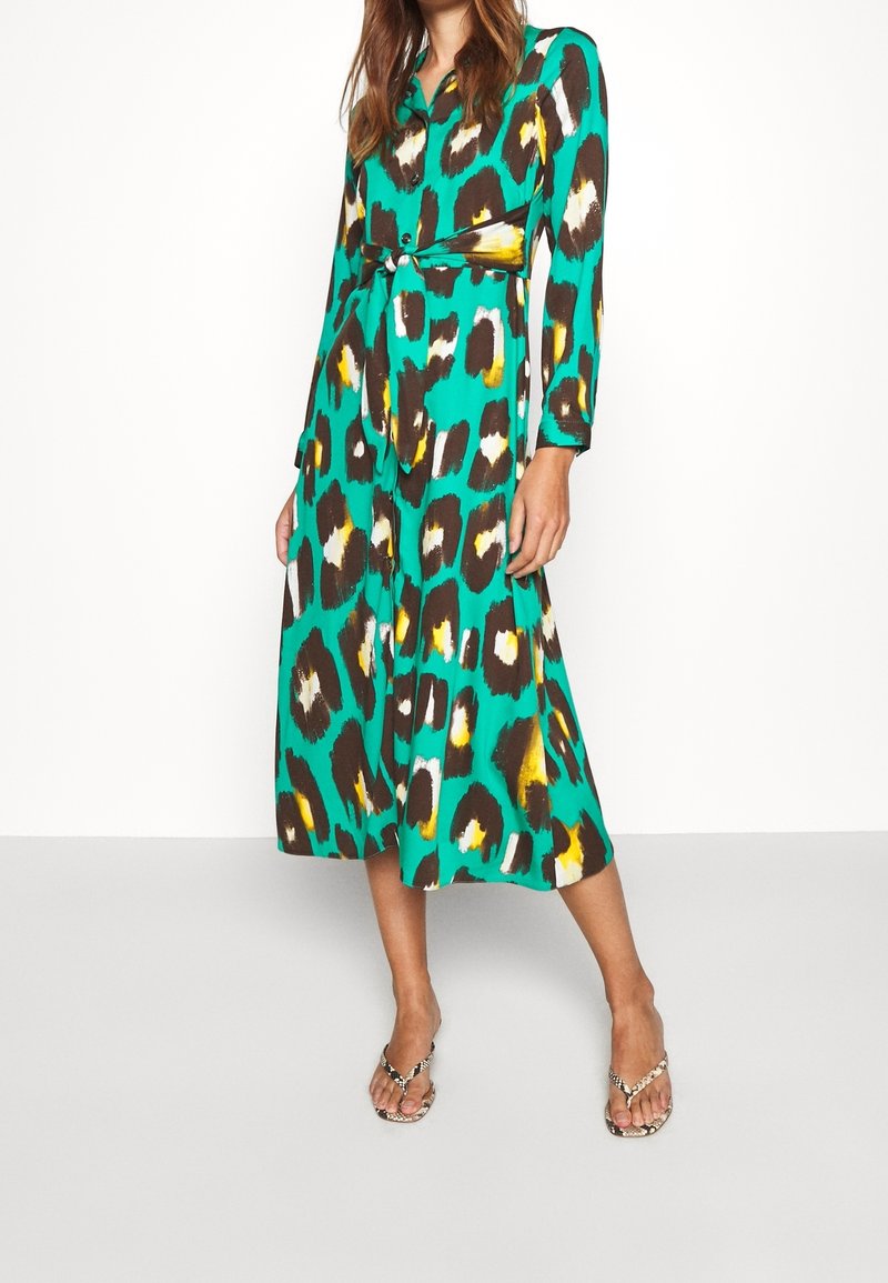 Robe longue boutonnée de couleur sarcelle avec un motif léopard en brun, jaune et blanc. Comprend une taille ceinturée et des manches longues.