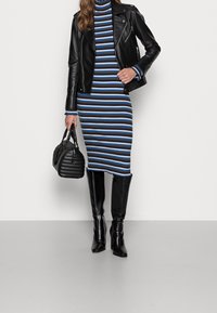 Svart läderbikerjacka över en ribbad, randig klänning i brunt, blått och vitt. Svarta knähöga stövlar och en texturerad svart handväska.