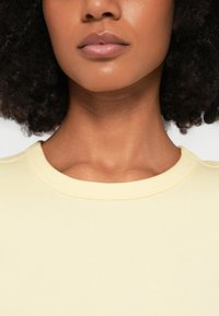 Ανοιχτόκίτρινη ριπ κοντομάνικη μπλούζα με στρογγυλή λαιμόκοψη, με λεία υφή. Το ύφασμα φαίνεται ελαστικό και εφαρμοστό γύρω από το γιακά.