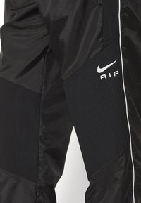 Schwarze Nike-Jogginghose mit einer Kombination aus glänzenden und strukturierten Materialien. Enthält ein auffälliges weißes "AIR"-Logo und kontrastierende weiße Seitenstreifen.