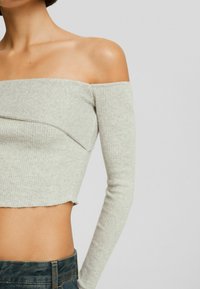 Jasnoszara bluzka typu off-the-shoulder z długimi rękawami, z prążkowaną teksturą i skróconym fasonem z surowym wykończeniem dołu.