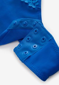 Mėlynos medžiagos drabužis su lygiu paviršiumi, turintis kelis mėlynos spalvos spaustukus ir gėlių nėrinių detalę viršutinėje dalyje.