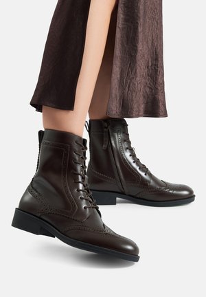 Brązowe skórzane botki do kostki z ażurowym wzorem, zawiązywane na sznurowadła i zamkiem błyskawicznym po boku. Teksturowana powierzchnia i niski, blokowy obcas.