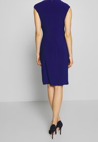 Marinblå ärmlös klänning med en figurnära design, knälång fåll och bakfållar. Avslutad med en dold dragkedja på baksidan.