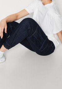 Mörkblå denim-joggers med elastiska muddar, sidofickor och synliga sömmar, i kombination med en löst sittande vit t-shirt och vita skor.