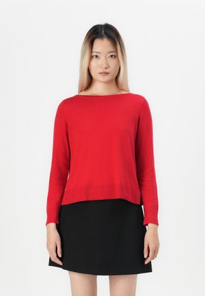 Maglione rosso a maniche lunghe lavorato a maglia con scollatura ampia e orlo a coste, abbinato a un vestito nero, su uno sfondo bianco.