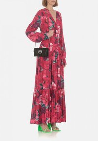 Lungo vestito floreale rosa con maniche lunghe, dettagli con bottoni e gonna a strati. Abbinato a una piccola borsa nera e sandali con tacco verdi.