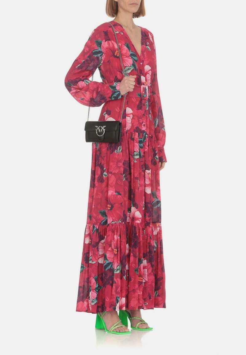 Lungo vestito floreale rosa con maniche lunghe, dettagli con bottoni e gonna a strati. Abbinato a una piccola borsa nera e sandali con tacco verdi.