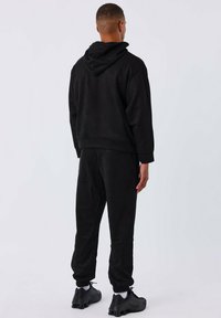 Chándal de forro polar negro con sudadera con capucha y puños elásticos, que presenta un ajuste holgado y una textura suave. Mostrado desde la parte de atrás.