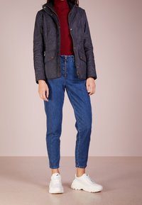 Černá prošívaná bunda s kapucí, dvěma předními kapsami, zlatým zipem, kombinovaná s džíny s vysokým pasem a bílými teniskami.