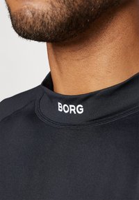 Juoda sportinė marškinėliai su aukštu apykakle, dekoruoti baltais rašmenimis "BORG" prie kaklo. Sklandus paviršius ir prigludęs dizainas.