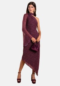 Asymmetrisches lila Kleid mit einem Ärmeldesign, strukturiertem Stoff, kombiniert mit einer dunkel-lila Handtasche und Plateau-Heels.