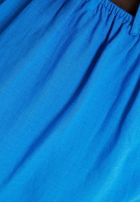 Modrá látka s řaseným elastickým pasem, ukazující texturu a jemné záhyby.