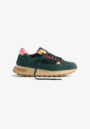 Zapatilla verde oscuro con acentos en rosa y amarillo, paneles de malla, suela marrón claro y un cordón verde deshecho sobre un fondo blanco.