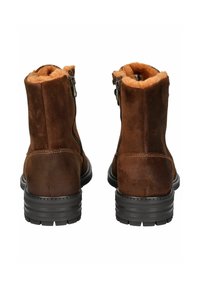 Botas de tobillo de ante marrón con forro de pelo sintético, cierre de cremallera en el lateral y suelas de goma negra texturizada con un diseño de tacón apilado.