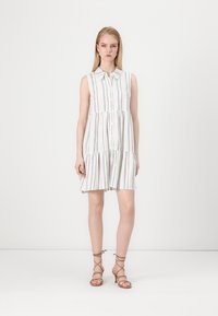 Robe sans manches blanche avec des rayures verticales bleues, devant boutonné, jupe froncée et coupe décontractée. Portez-la avec des sandales bronzées à lanières.