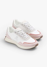 Bílé tenisky s růžovým semišovým overlayem, se znakem lebky, šněrováním a červenými akcenty na bocích a u špičky. Texturovaná gumová podrážka.