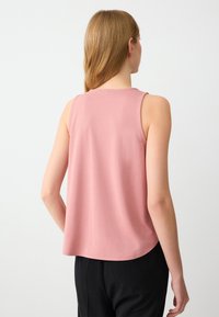 Top rosa senza maniche realizzato in tessuto liscio, con scollatura rotonda e orlo curvato, abbinato a pantaloni neri.