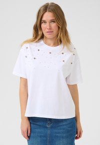 T-shirt en coton blanc à coupe décontractée, avec des clous métalliques disposés en motif éparpillé sur le devant. Manches courtes et col rond.