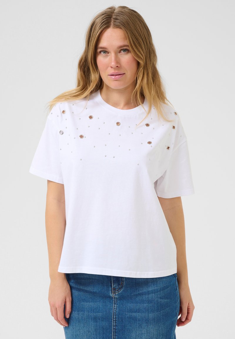 T-shirt en coton blanc à coupe décontractée, avec des clous métalliques disposés en motif éparpillé sur le devant. Manches courtes et col rond.