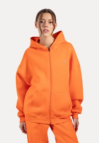 Lys orange zip-up hættetrøje med en stor h�ætte, kengurulommer, ribbede manchetter og en afslappet pasform. Blødt stof med en glat tekstur.