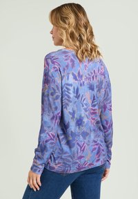 Maglietta a maniche lunghe in tonalità di blu con un motivo floreale, realizzata in tessuto testurizzato e dalla vestibilità rilassata, abbinata a jeans blu scuro.