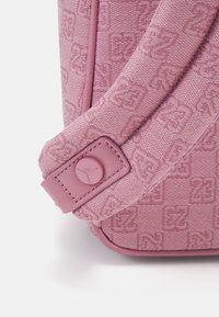 Ροζ υφασμάτινο σα�κίδιο με καρό μοτίβο που διαθέτει ανάγλυφα σχέδια, ραμμένο λουράκι και κυκλικό λογότυπο στη μία πλευρά.