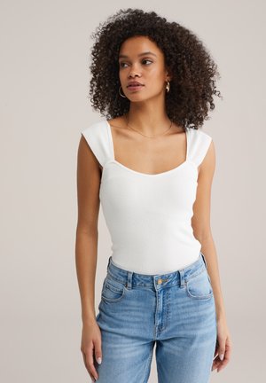 Fehér bordázott body négyzet alakú nyakkivágással és széles pántokkal, magas derekú kék farmernadrággal párosítva, elülső zsebekkel és gombos záródással.