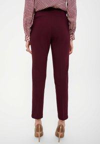 Pantalon bordeaux ajusté avec une coupe slim. Texture lisse, taille mi-haute et deux poches arrière. Associé à des talons de couleur neutre.