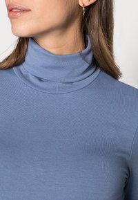 Maglione a collo alto blu con una texture morbida a costine e un design aderente, che mette in risalto un collo alto e linee pulite.