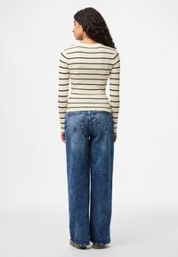 �Μπεζ ριμπ μπλούζα με μακρύ μανίκι και μαύρες οριζόντιες ρίγες, συνδυασμένη με χαλαρές μπλε τζιν παντελόνες, που επιδεικνύουν ίσια πόδια και παραδοσιακές τσέπες.