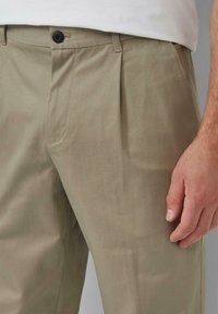 Khaki spodnie z gładką fakturą, z plisowanym przodem, z zapięciem na guzik i kieszeniami bocznymi, w komplecie z białą bluzką.