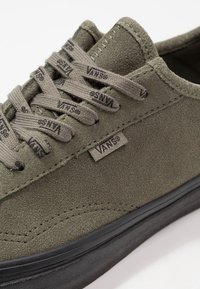 Tenisová bota z olivově zelené broušené kůže s tmavou gumovou podrážkou, s černými tkaničkami s označením a štítkem Vans na boku. Minimalistický design.