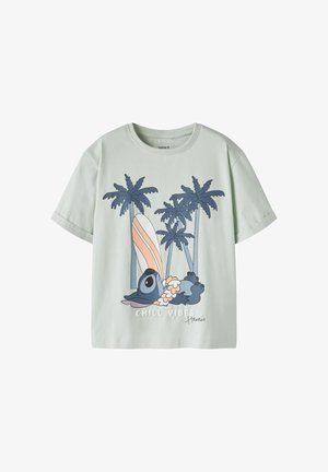 Chemise vert clair à manches courtes avec un koala bleu dessin animé allongé sous des palmiers, une planche de surf rayée, le texte « CHILL VIBES » et la signature « Hawaii ».